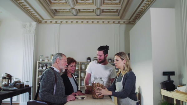 Senior couple customers buying groceries in zero waste shop, sales assistants serving them.