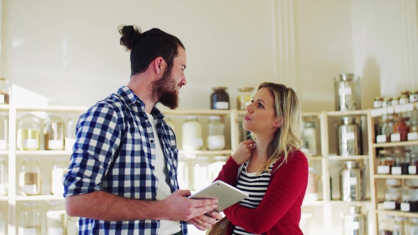 Young male shop assistant with tablet serving an attractive woman in a zero waste shop.