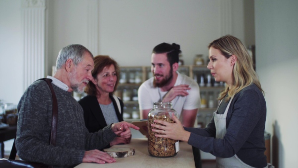 Senior couple customers buying groceries in zero waste shop, sales assistants serving them.