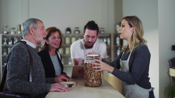 Senior couple customers buying groceries in zero waste shop, sales assistants serving them.