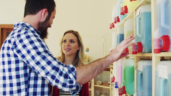 Young male shop assistant serving an attractive woman in a zero waste shop.