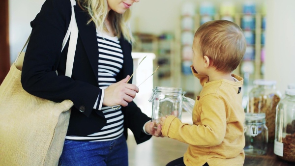 An attractive young woman with a toddler boy buying groceries in zero waste shop. Slow motion.