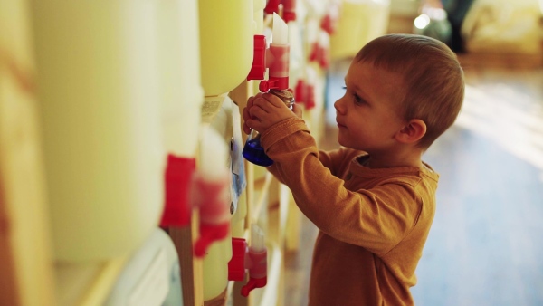 A cute small toddler boy standing by dispensers in zero waste shop. Slow motion.