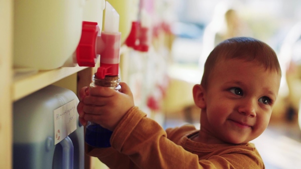 A close-up of cute small toddler boy standing by dispensers in zero waste shop. Slow motion.