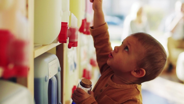 A cute small toddler boy standing by dispensers in zero waste shop. Slow motion.