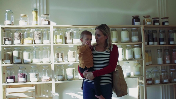 An attractive young woman walking with a toddler boy in zero waste shop, talking to him. Slow motion.