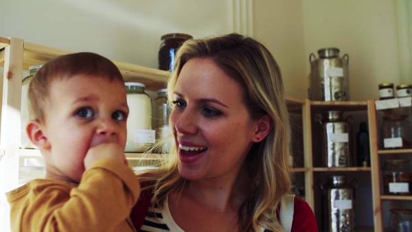 An attractive young woman walking with a toddler boy in zero waste shop, talking to him. Slow motion.