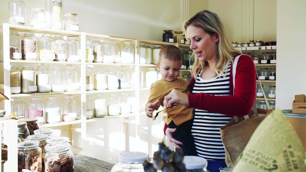 An attractive young woman with a toddler boy buying groceries in zero waste shop. Slow motion.