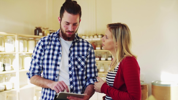 Young male shop assistant with tablet serving an attractive woman in a zero waste shop.