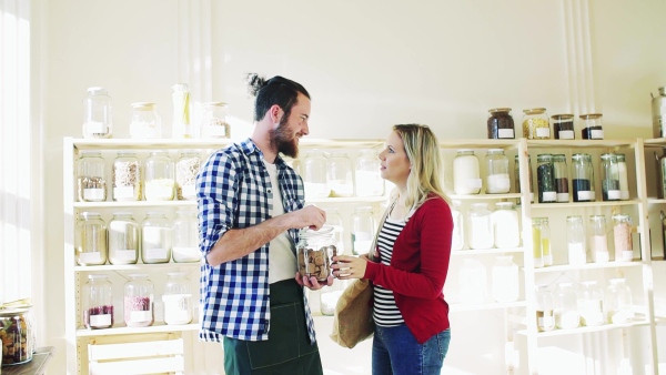 Young male shop assistant serving an attractive woman in a zero waste shop. Slow motion.