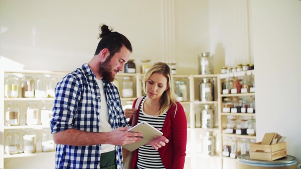 Young male shop assistant with tablet serving an attractive woman in a zero waste shop. Slow motion.