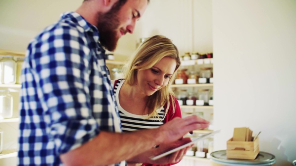 Young male shop assistant with tablet serving an attractive woman in a zero waste shop. Slow motion.