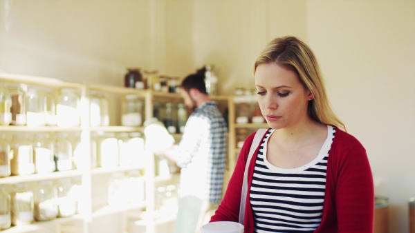 Young male shop assistant with tablet serving an attractive woman in a zero waste shop.