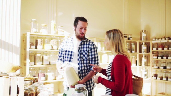 Young male shop assistant serving an attractive woman in a zero waste shop. Slow motion.