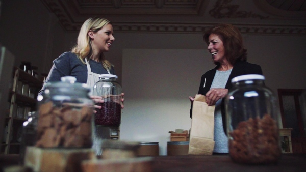 A young female shop assistant serving a senior customer in a zero-waste shop. Slow motion.