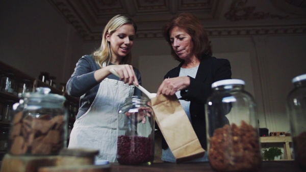 A young female shop assistant serving a senior customer in a zero-waste shop. Slow motion.