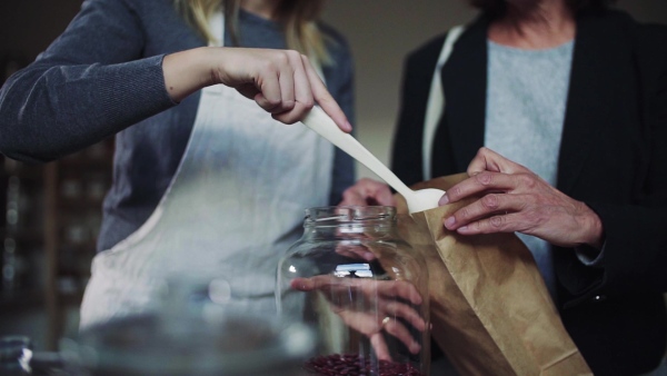 A midsection of young female shop assistant serving a senior customer in a zero-waste shop. Slow motion.