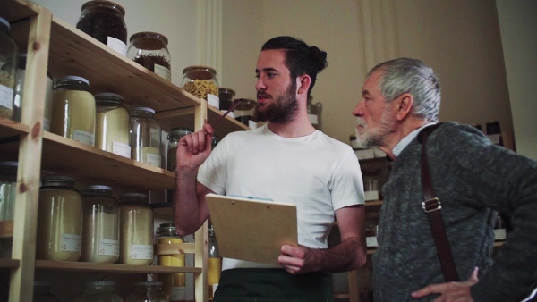 Young shop assistant serving a senior man customer in a zero waste shop. Slow motion.