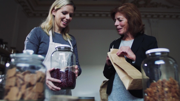 A young female shop assistant serving a senior customer in a zero-waste shop.