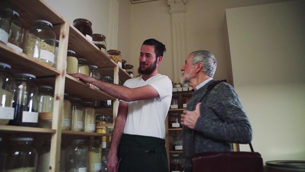 Young shop assistant serving a senior man customer in a zero waste shop. Slow motion.