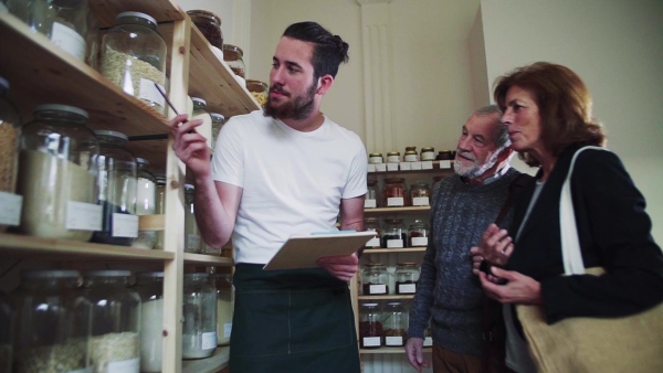 Young shop assistant serving a senior couple customers in a zero waste shop. Slow motion.