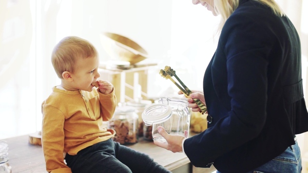 An unrecognizable young woman with a toddler boy buying biscuits in zero waste shop. Slow motion.