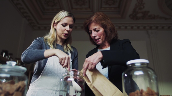 A young female shop assistant serving a senior customer in a zero-waste shop.