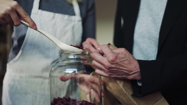 A midsection of young female shop assistant serving a senior customer in a zero-waste shop.