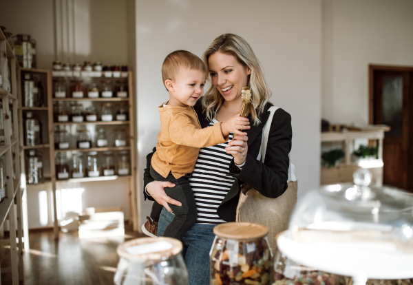 An attractive young woman with a toddler boy buying groceries in zero waste shop.