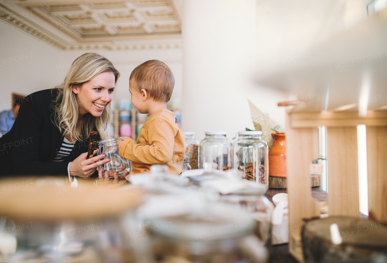 An attractive young woman with a toddler boy buying groceries in zero waste shop.