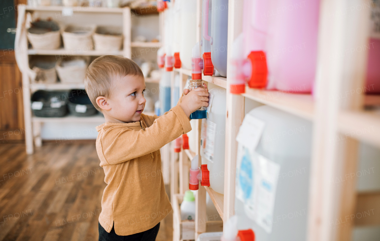 A cute small toddler boy standing by dispensers in zero waste shop.