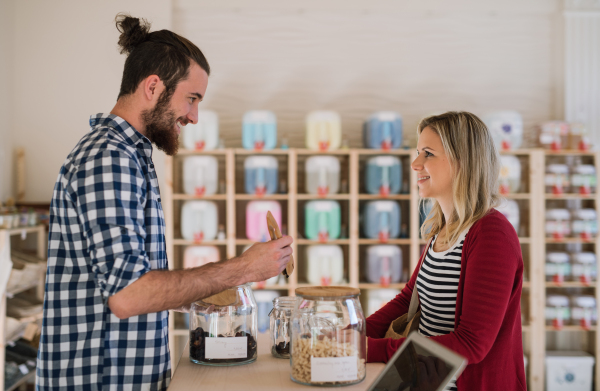 Young handsome male shop assistant serving a female customer in a zero waste shop.