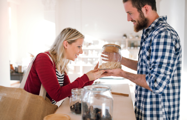 Young male shop assistant serving an attractive woman in a zero waste shop.