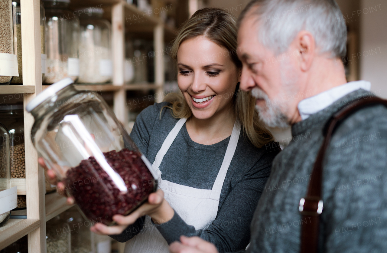 Young female shop assistant serving a senior man customer in a zero waste shop.