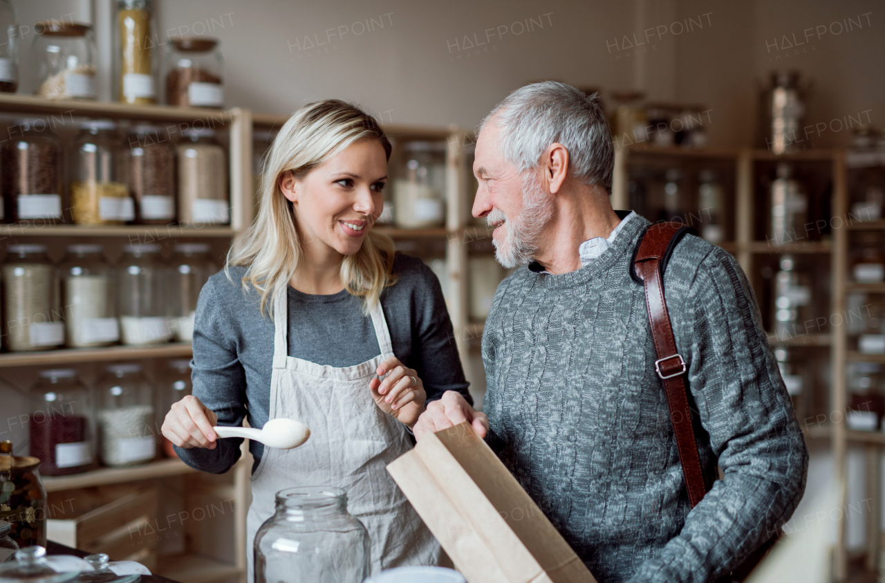 Young female shop assistant serving a senior man customer in a zero waste shop.