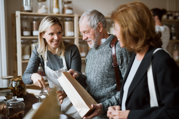 A young female shop assistant serving a senior couple in a zero-waste shop.