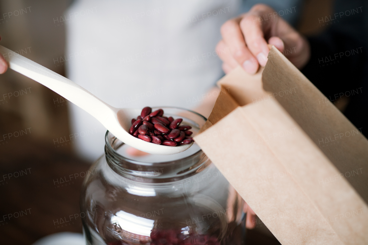 A midsection of a customer buying groceries in a zero waste shop, unrecognizable shop assitant putting beans in a paper bag. A close-up.