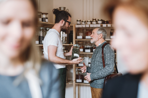 Young shop assistant serving a senior man customer in a zero waste shop.