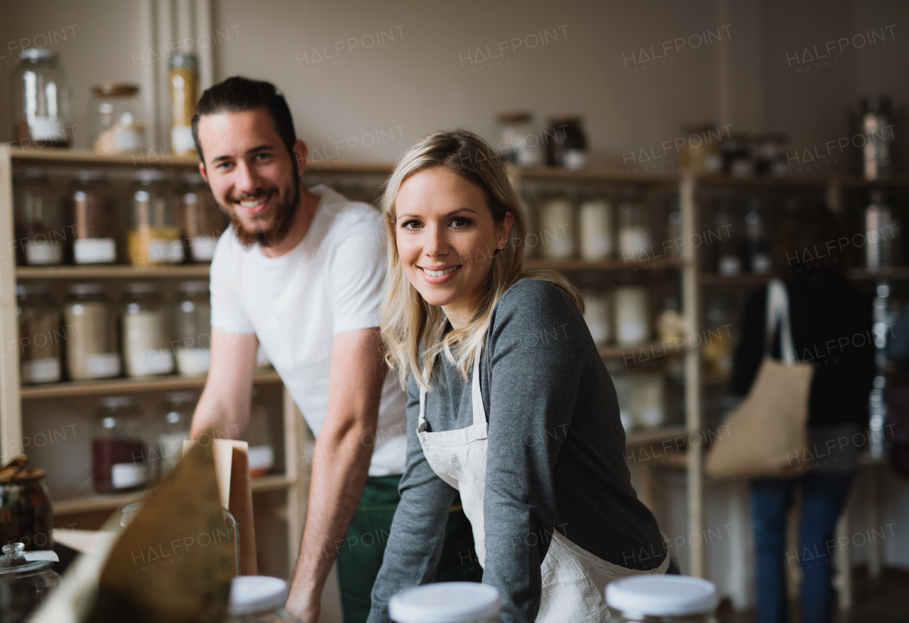 A portrait of two cheerful shop assistants standing in zero waste shop, looking at camera.