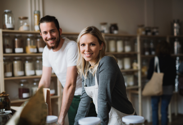 A portrait of two cheerful shop assistants standing in zero waste shop, looking at camera.