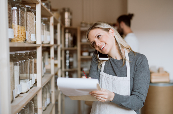 A female shop assistant with smartphone working in a zero-waste shop, checking stock.