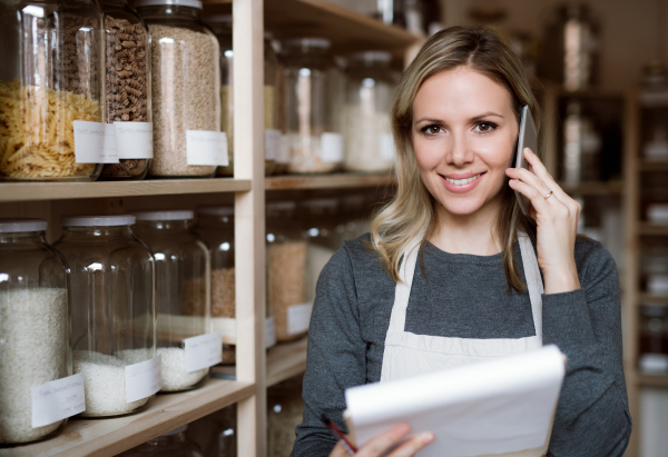 A female shop assistant with smartphone working in a zero-waste shop, checking and ordering stock.