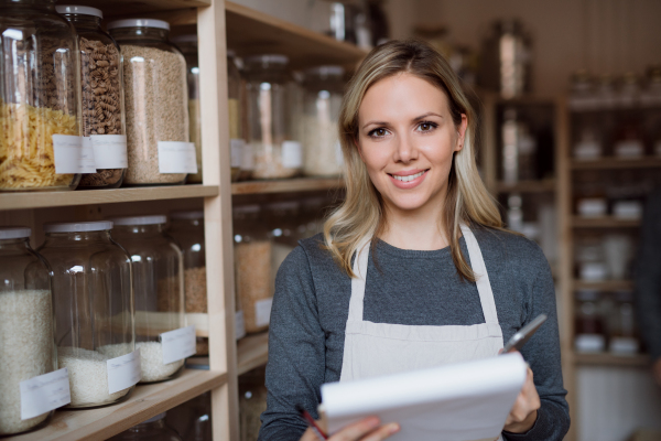 A female shop assistant with smartphone working in a zero-waste shop, checking and ordering stock.