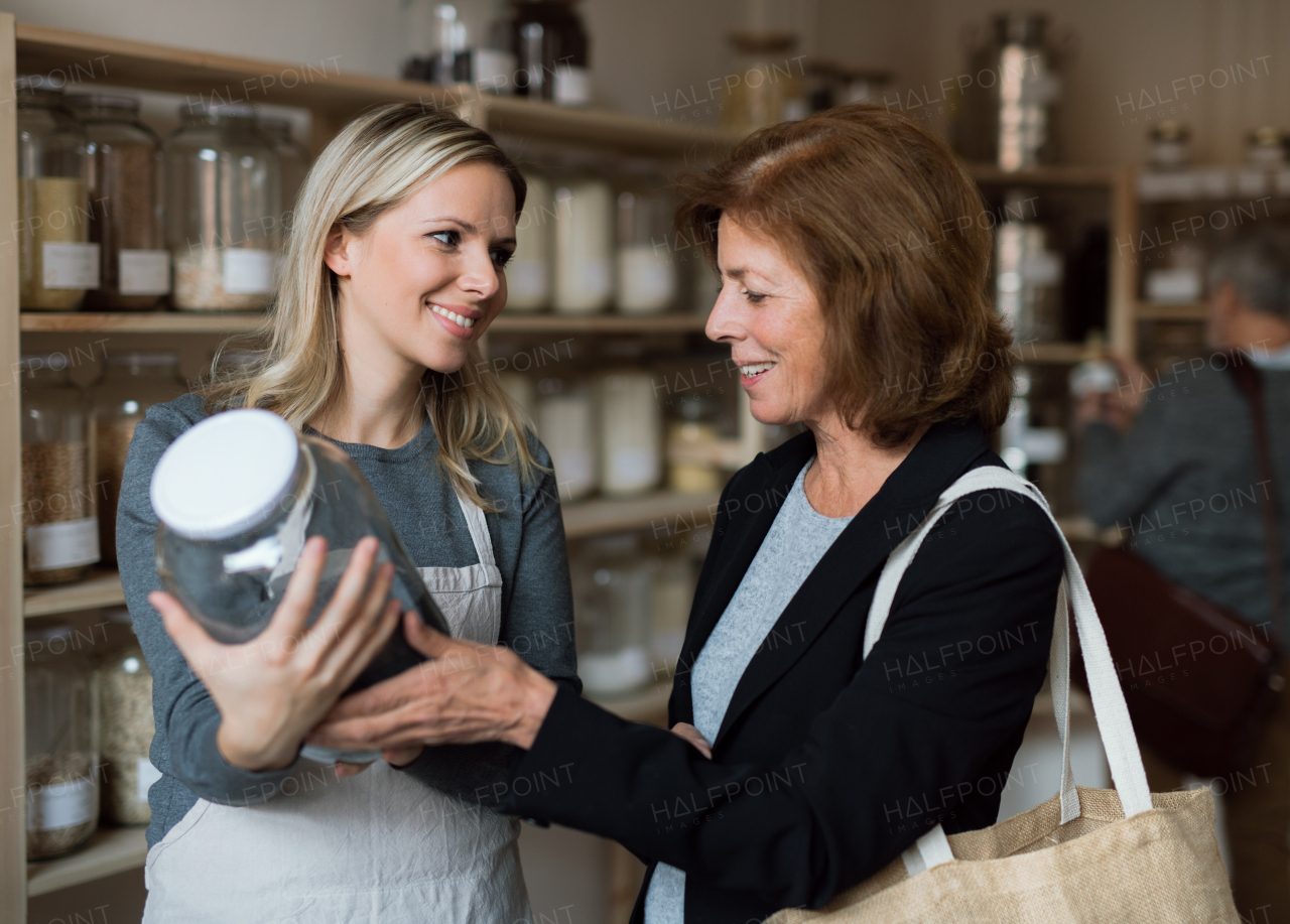 A young female shop assistant serving a senior customer in a zero-waste shop.