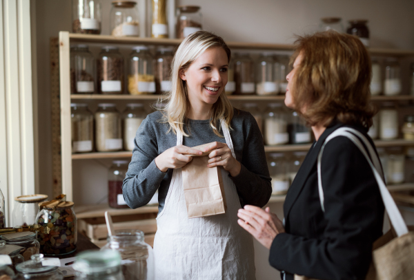 A young female shop assistant serving a senior customer in a zero-waste shop.