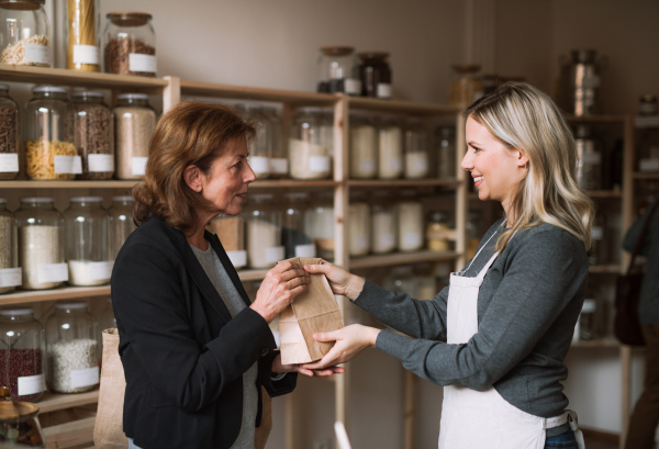 A young female shop assistant serving a senior customer in a zero-waste shop.