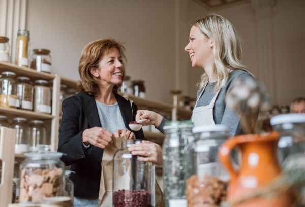 A young female shop assistant serving a senior customer in a zero-waste shop.