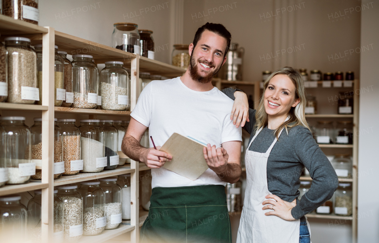 Two shop assistants standing in zero waste shop, checking and ordering stock.