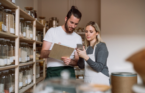 Two shop assistants standing at the counter in zero waste shop, checking and ordering stock.