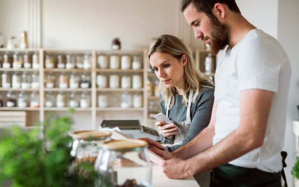 Two shop assistants standing at the counter in zero waste shop, checking and ordering stock.